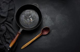 poêle ronde vide en fonte avec manche en bois sur tableau noir, vue de dessus photo