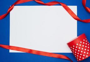 feuille de papier blanche vide et ruban torsadé de soie rouge sur fond bleu photo
