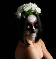 jeune belle fille avec masque de mort mexicain traditionnel. calavera catrina. maquillage de crâne de sucre. fille vêtue d'une couronne de roses blanches photo