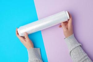 deux mains tiennent un grand rouleau de film transparent blanc enroulé pour emballer les aliments photo