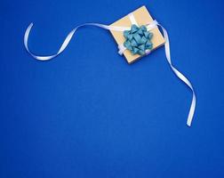 boîte carrée avec un cadeau attaché avec un ruban blanc avec un arc sur un fond classique bleu photo