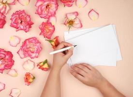 la fille tient dans sa main gauche un stylo blanc et signe des enveloppes sur un fond de pêche photo