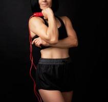 jeune femme avec une figure sportive en uniforme noir tient une corde rouge pour sauter photo