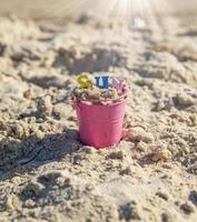 un seau en fer pour bébé rose rempli de lettres colorées en bois se dresse sur le sable photo