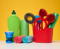 panier en plastique avec brosses, désinfectant dans une bouteille sur fond jaune. photo