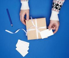 deux mains féminines tiennent une boîte cadeau carrée en carton attachée avec un ruban blanc et des cartes de visite en papier vides photo