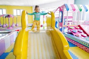fille heureuse jouant à l'aire de jeux intérieure du centre de jeux. coulissant dans le toboggan jaune. photo