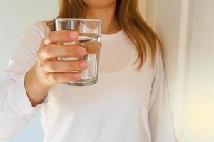une femme tenant un verre d'eau à boire. l'eau potable est bénéfique pour le corps. notion de bonne santé