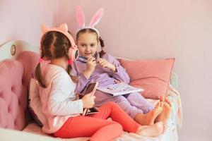 deux soeurs s'amusent à la maison, dessinent un lapin et écoutent de la musique dans des écouteurs, la fille plus âgée a un bandeau avec des oreilles de lapin sur la tête, attendant les vacances de pâques photo