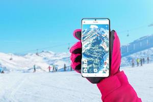 carte de ski sur téléphone intelligent dans la main de la femme avec un gant rose. concept d'application de ski et de snowboard pour le concept de suivi d'itinéraire et de distance. skieurs et pistes de ski en arrière-plan photo