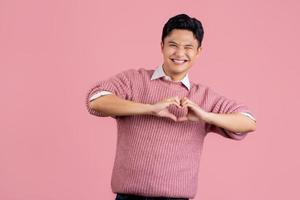 jeune homme asiatique portant un pull rose décontracté souriant amoureux faisant la forme de symbole de coeur avec les mains. notion romantique. photo