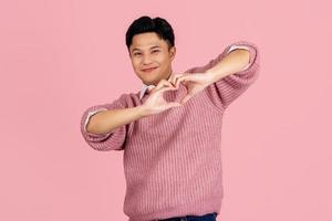 bel homme asiatique avec barbe portant un pull rose souriant amoureux faisant la forme de symbole de coeur avec les mains. notion romantique. photo
