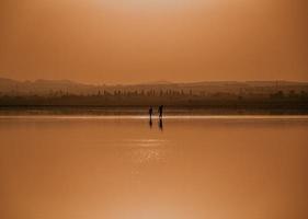 silhouette de 2 personnes debout sur un plan d'eau pendant le coucher du soleil photo