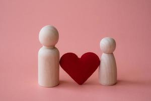 forme de coeur rouge entre figurines en bois d'homme et de femme sur fond rose. notion d'amour. photo