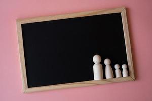 figurines en bois du père de famille, de la mère et des enfants sur le tableau noir sur fond rose. copier l'espace pour le texte. photo