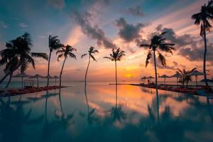 beau ciel au bord de la piscine et au coucher du soleil. paysage de plage tropicale luxueux, chaises longues et chaises longues et réflexion de l'eau. réflexion des palmiers, incroyable paysage de plage d'été de luxe. coucher de soleil sur la plage photo