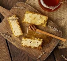 Nid d'abeille de cire avec du miel sur planche de bois et cuillère en bois, table marron, vue de dessus photo