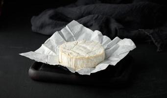 fromage brie rond sur un papier froissé blanc, table en bois photo