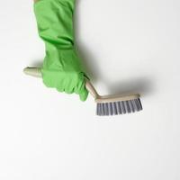 la main dans un gant de nettoyage en caoutchouc vert tient une brosse en plastique sur un fond blanc photo