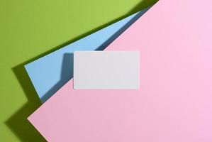 carte de visite rectangulaire vierge se trouve sur un fond vert clair moderne avec des feuilles de papier bleu et rose avec une ombre photo