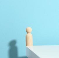 figurine en bois d'un homme sur fond bleu avec une ombre. le concept de solitude, de tristesse photo