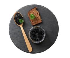 caviar de paddlefish noir dans une cuillère en bois, une tranche de pain et un pot sur une planche en graphite ronde noire photo