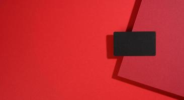 carte de visite rectangulaire noire vierge se trouve sur un fond rouge moderne avec des feuilles de papier rouges avec une ombre. modèle d'entreprise photo