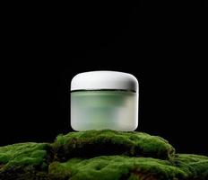 pot en plastique vert rond avec couvercle blanc pour cosmétiques se dresse sur mousse verte, fond noir. crèmes et masques naturels. l'image de marque du produit photo