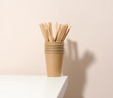 gobelets en carton en papier brun et bâtonnets d'agitation en bois sur une table blanche, fond beige. vaisselle écologique, zéro déchet photo