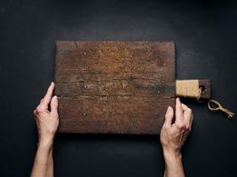 planche à découper en bois vide dans les mains des femmes sur une table en bois noir, vue de dessus photo