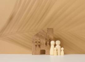 figurines familiales en bois, maison modèle sur fond marron. achat immobilier, concept de location. emménager dans de nouveaux appartements photo