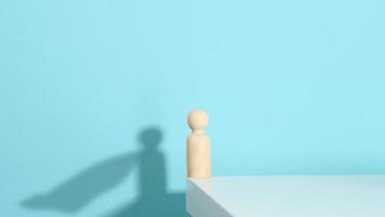 figurine en bois d'un homme et d'une ombre avec un manteau en développement, le concept du fort et du gagnant. tout le monde est plus fort qu'il ne le pense, un super-héros. fond bleu photo