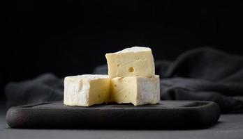 fromage brie rond sur une planche à découper en bois marron, fond noir