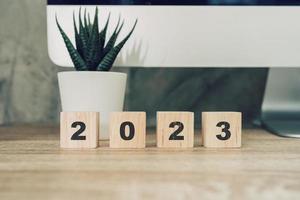 Bonne année 2023 sur un bloc de bois sur un ordinateur de bureau de table en bois et une plante en pot. notion de nouvel an photo