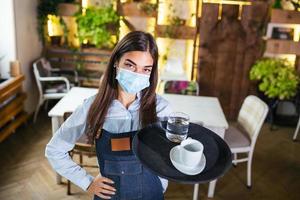 une serveuse dans un masque de protection médicale sert le café au restaurant pendant la pandémie de coronavirus représentant un nouveau concept normal photo