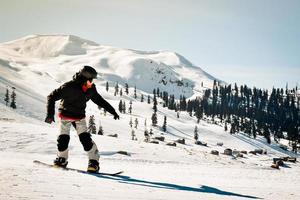 snowboarder heureux vêtu de vêtements de sport noir foncé descendant la pente de la montagne en géorgie, goderdzi le jour ensoleillé du caucase photo