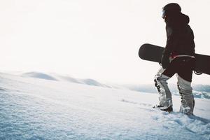 snowboarder marchant avec snowboard au coucher du soleil dans les montagnes enneigées. fond cinématographique de snowboarder freerider solo photo