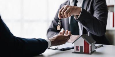 les agents immobiliers s'engagent à acheter une maison et à remettre les clés aux clients dans les bureaux de leur agence. accord de concept photo