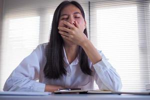 une femme d'affaires asiatique bâille et s'endort en travaillant et en faisant des recherches au bureau. photo