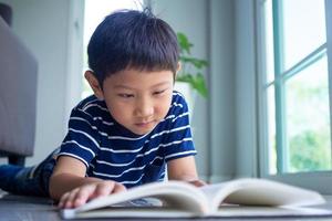 le petit garçon lit un livre dans la maison. apprendre à la maison photo