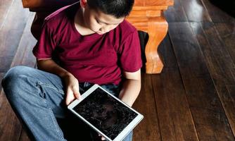 portrait d'un petit garçon asiatique, enfant visage triste, enfant malheureux assis tenant une tablette cassée, émotion visage triste et triste, concept d'enfants déprimés photo