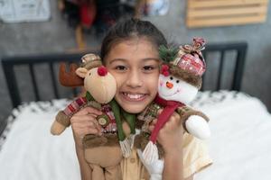 douce petite fille étreint un ours en peluche, regarde la caméra et sourit assise sur son lit à la maison. photo