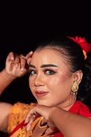 un regard aigu d'une femme indonésienne avec du maquillage sur son visage tout en portant une robe orange et des boucles d'oreilles dorées photo