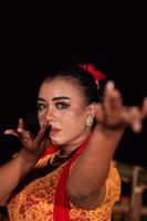 le visage féroce d'une femme balinaise avec du maquillage dans une robe orange traditionnelle et une écharpe rouge tout en dansant au festival photo