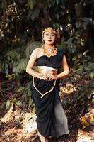 belle femme asiatique debout dans une robe noire tout en portant une couronne dorée et une chaîne dorée à l'intérieur de la forêt photo