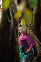 femme asiatique prend une pose de danse dans la jungle tout en portant une robe violette et un collier doré avec un beau sourire photo