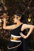 une belle javanaise pose avec sa main dans un costume noir tout en portant une couronne dorée et un collier doré