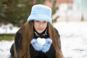 une belle fille dans un chapeau de fourrure et des mitaines tient une boule de neige dans ses mains. photo