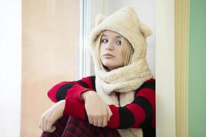 une adolescente dans un drôle de chapeau de fourrure est assise sur le rebord de la fenêtre et regarde la caméra. photo