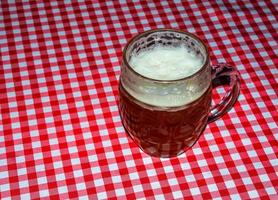 une chope de bière sur une table recouverte d'une nappe à carreaux rouge. photo